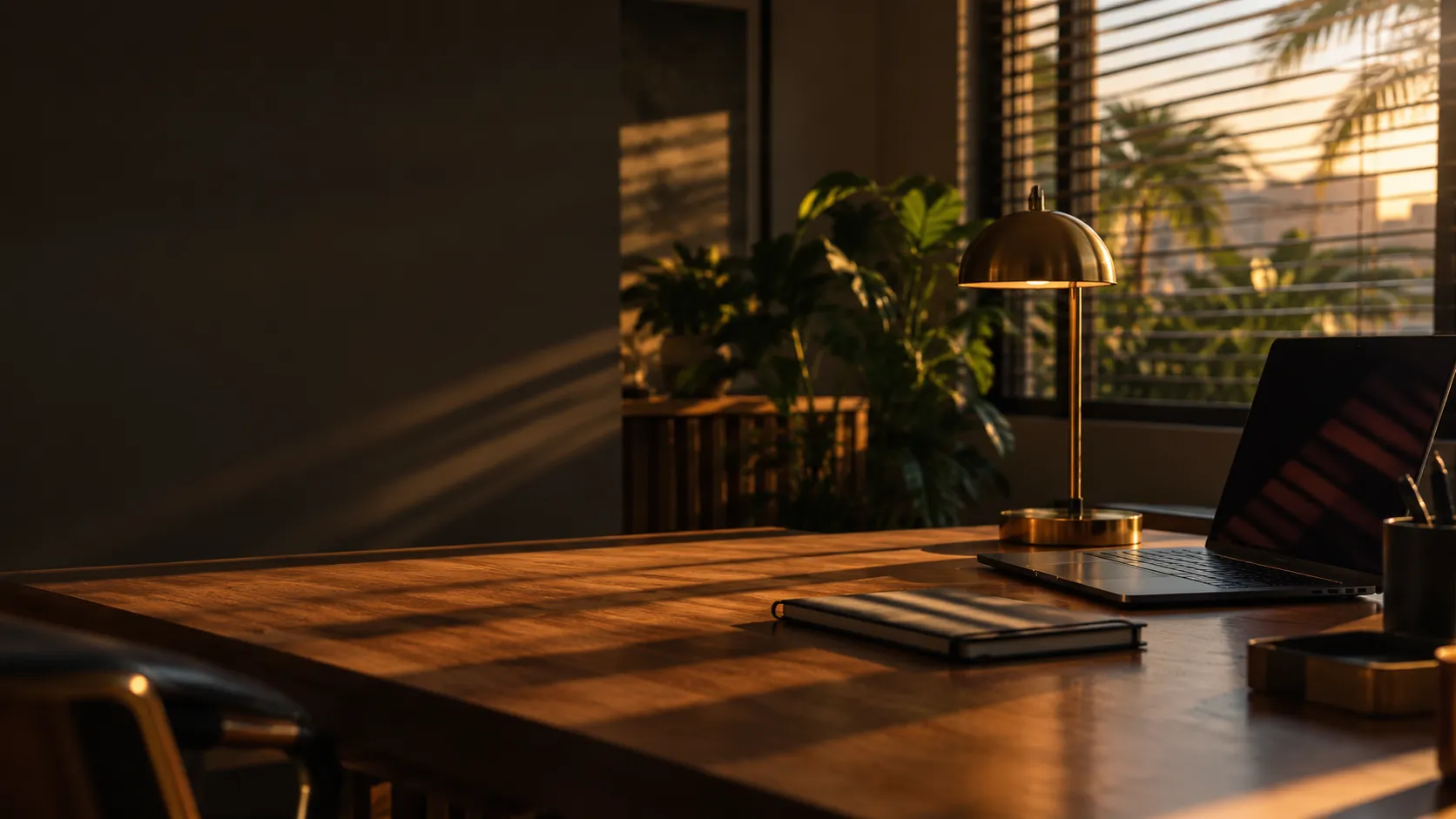 Mesa de trabalho organizada ao entardecer, com luz recortada pela persiana